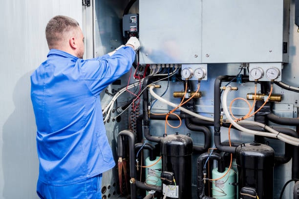 HVAC technician in blue uniform servicing commercial refrigeration unit with gauges and electrical components, emphasizing expert maintenance and repair services for businesses.