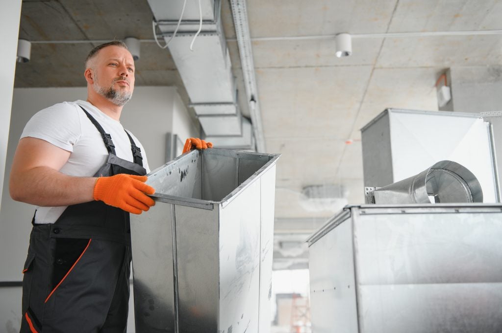 Repairman in work gloves holding ventilation duct, focused on air duct cleaning for improved indoor air quality in commercial spaces.