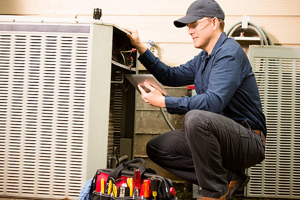 HVAC technician inspecting commercial air conditioning unit, using tablet and tools for maintenance, emphasizing professional HVAC services in Brooklyn.