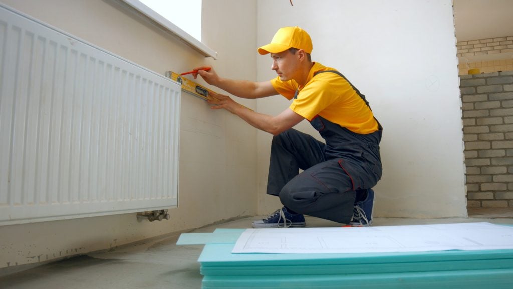 HVAC technician installing baseboard heater in commercial space, ensuring level alignment and proper placement for efficient heating.