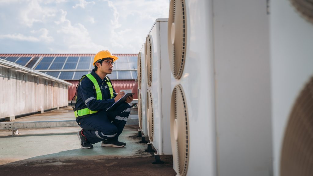 Technician in safety gear inspecting commercial air conditioning units on a rooftop, emphasizing HVAC maintenance and reliability for Brooklyn businesses.