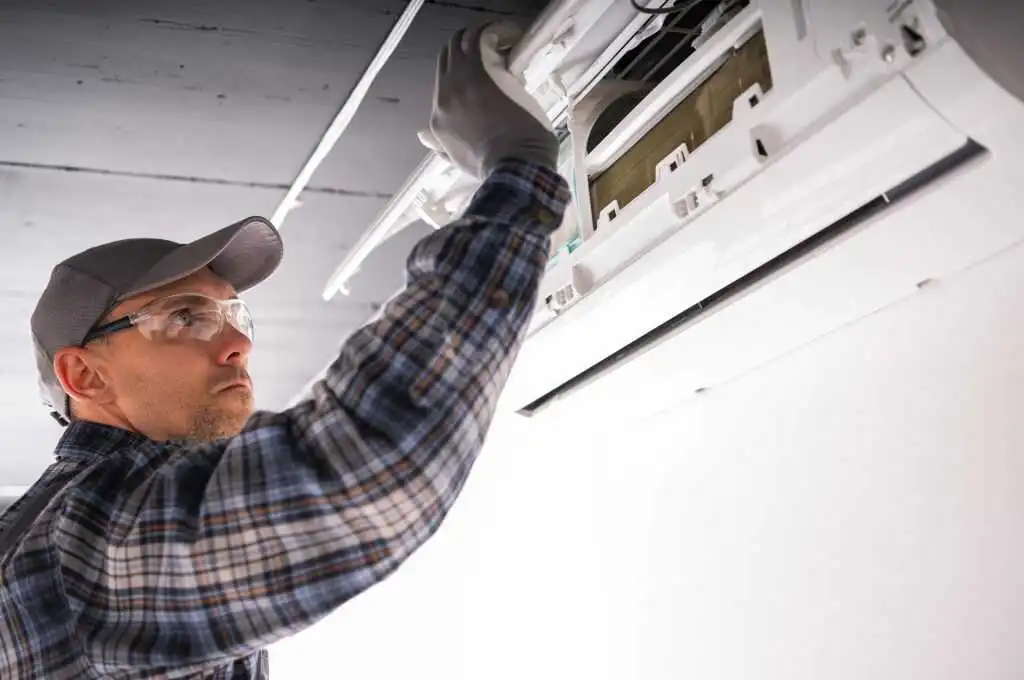 Heating technician performing maintenance on a ductless heat pump in a commercial space, wearing safety goggles and gloves, focused on ensuring energy-efficient heating solutions for Brooklyn properties.