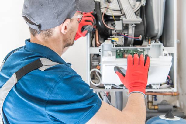 Technician in blue shirt and red gloves performing maintenance on a commercial furnace, focusing on internal components and wiring for efficient heating solutions.