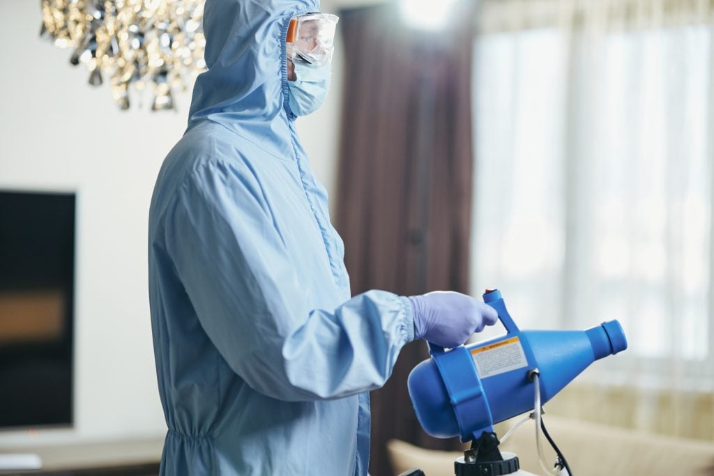 Technician in protective gear using a disinfectant sprayer to improve indoor air quality during commercial air cleaning installation in Brooklyn.